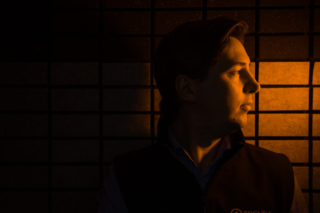 En man såt i ett mörkt utrymme och blickar mot en orange ljuskälla utanför bilden